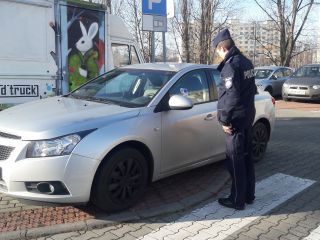 Policjant przy nieprawidłowo zaparkowanym samochodzie