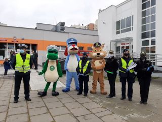 Strażnicy miejscy, policjanci oraz mundurowe maskotki - Ryś, Sznupek i Krododyl przed budynkiem szkoły