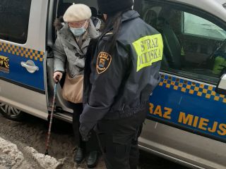 Strażniczka miejska pomaga wysiąść seniorce z radiowozu