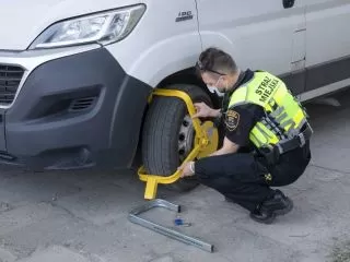 Strażnik miejski zakłada blokadę na koło samochodu